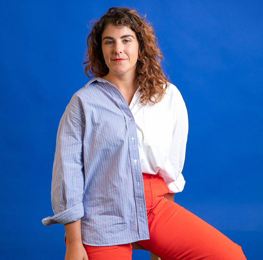 headshot of allison sitting on a stool in a two tone dress shirt and orange pants on a blue background